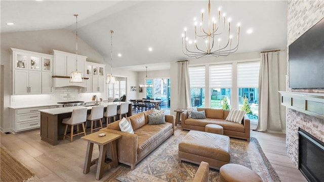 living room featuring light wood finished floors, a fireplace, high vaulted ceiling, and an inviting chandelier