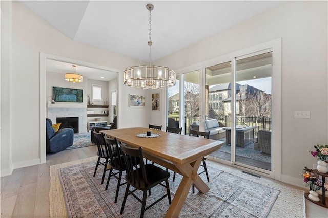 dining room with a fireplace, a healthy amount of sunlight, light wood finished floors, and a chandelier