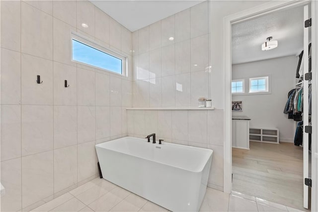 full bathroom with a wealth of natural light, a soaking tub, a spacious closet, and tile walls