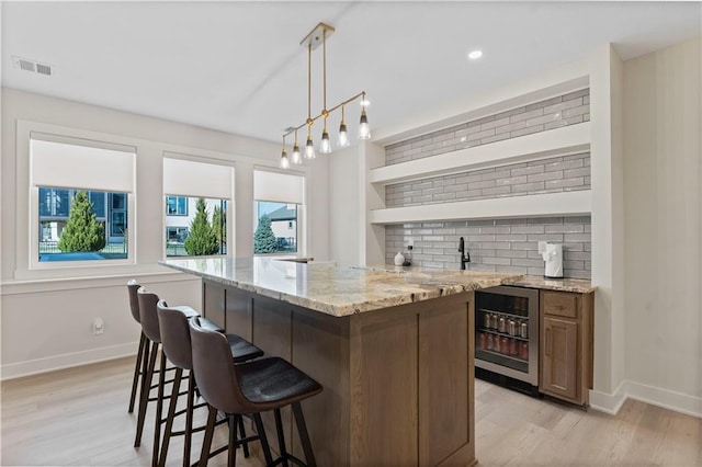 bar with tasteful backsplash, visible vents, wine cooler, indoor wet bar, and light wood-style floors