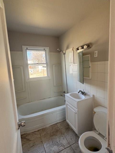 bathroom featuring tile patterned flooring, washtub / shower combination, toilet, vanity, and tile walls