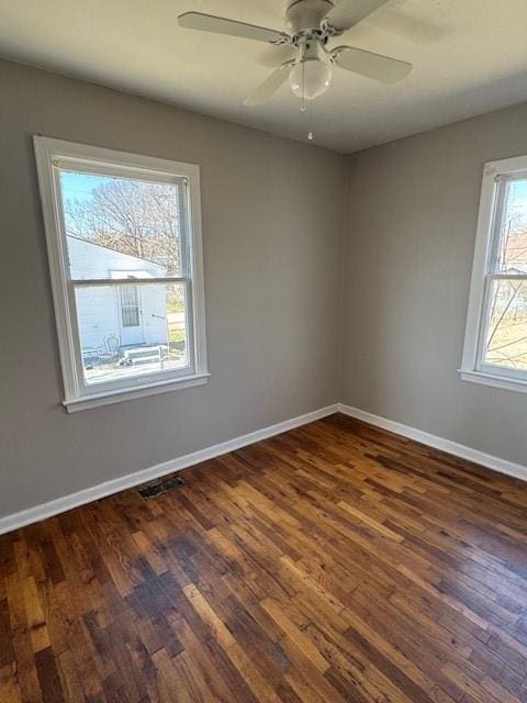 spare room featuring visible vents, a ceiling fan, baseboards, and dark wood-style flooring