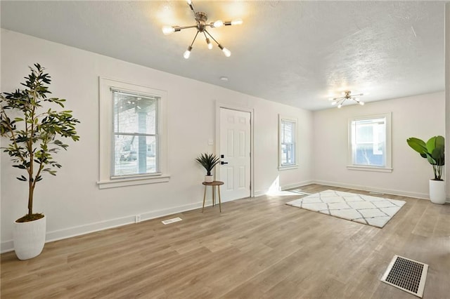 entrance foyer with visible vents, a notable chandelier, a textured ceiling, light wood-style floors, and baseboards