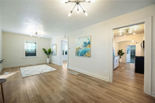 foyer entrance with light wood-style flooring, a textured ceiling, and an inviting chandelier