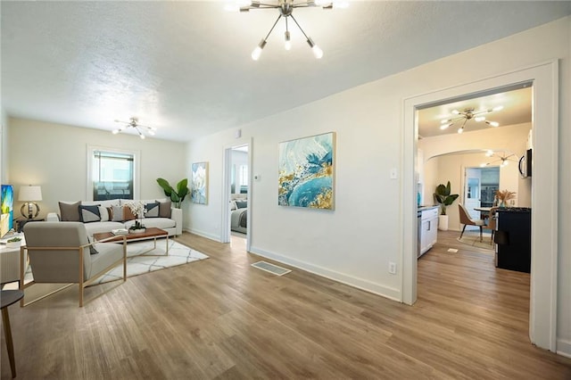 living room featuring a textured ceiling, a chandelier, and light wood finished floors