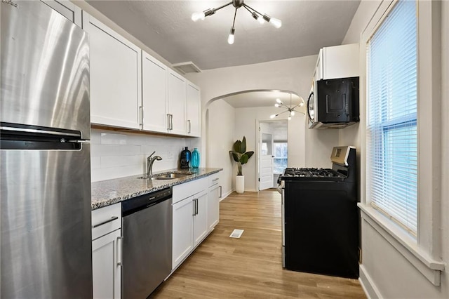 kitchen with a chandelier, stone counters, appliances with stainless steel finishes, arched walkways, and a sink