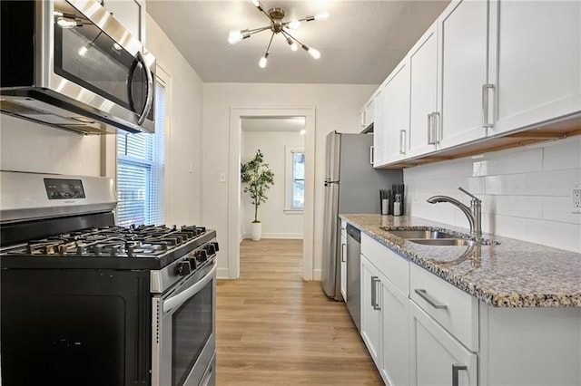 kitchen featuring a sink, light wood-style floors, appliances with stainless steel finishes, a notable chandelier, and tasteful backsplash