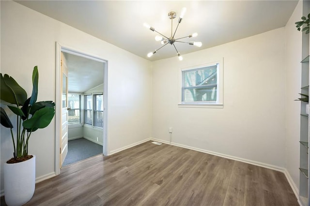 spare room with a chandelier, baseboards, and wood finished floors