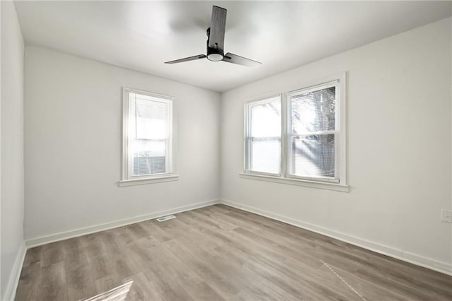 spare room featuring a ceiling fan, visible vents, light wood-style floors, and baseboards