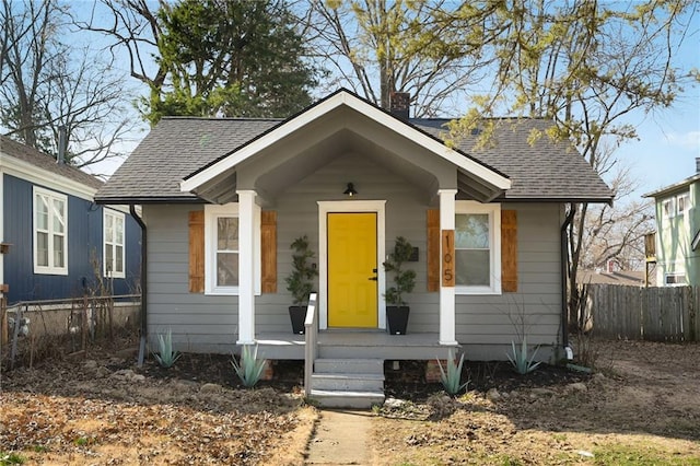 bungalow-style house with a porch, fence, roof with shingles, and a chimney