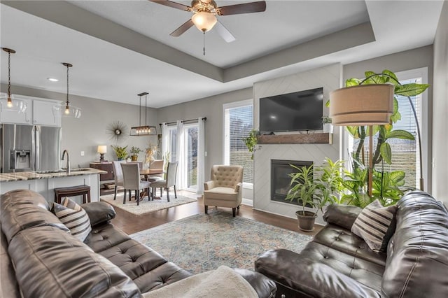 living room with a raised ceiling, a fireplace, wood finished floors, and a ceiling fan