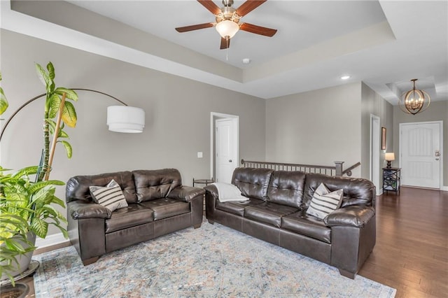 living area with ceiling fan with notable chandelier, a raised ceiling, baseboards, and wood finished floors