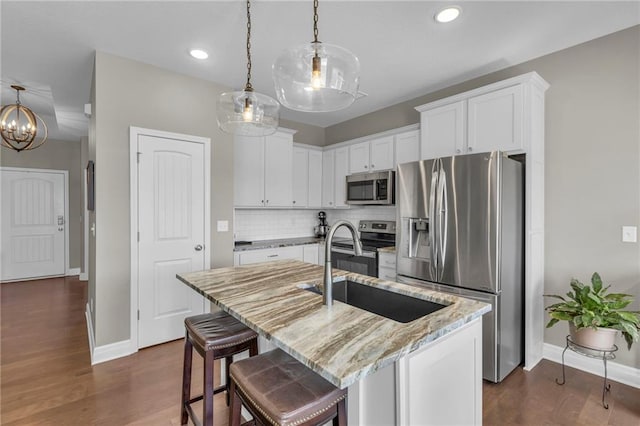 kitchen with a sink, backsplash, stainless steel appliances, light stone countertops, and a chandelier