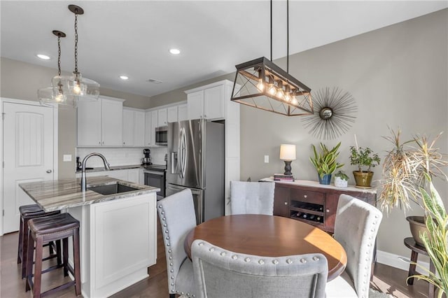 kitchen featuring backsplash, light stone countertops, appliances with stainless steel finishes, white cabinets, and a sink