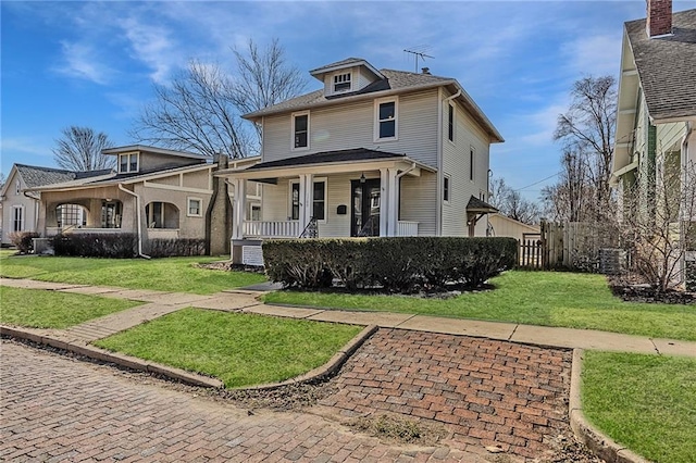 american foursquare style home featuring a front lawn, fence, and covered porch