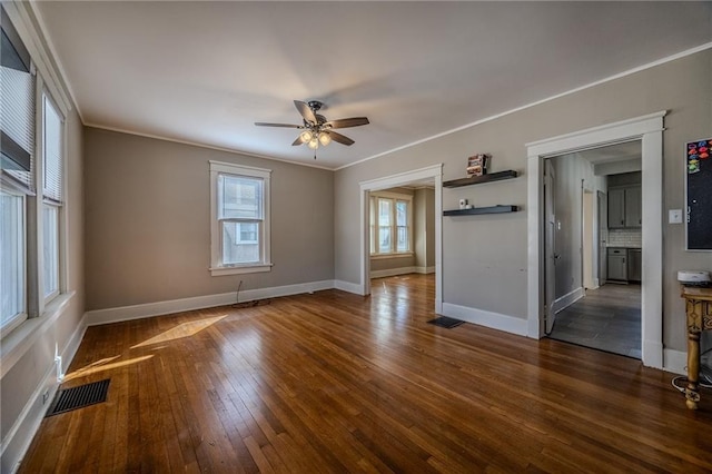 empty room with visible vents, baseboards, ornamental molding, and dark wood-style flooring