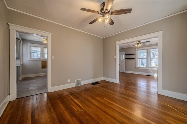 empty room with visible vents, wood-type flooring, baseboards, and ornamental molding