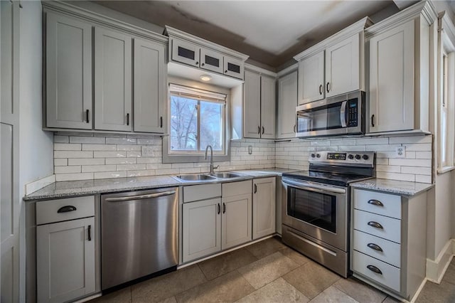 kitchen with a sink, decorative backsplash, light stone counters, and stainless steel appliances