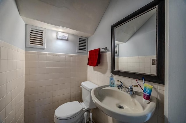 half bathroom with visible vents, toilet, a sink, tile walls, and lofted ceiling