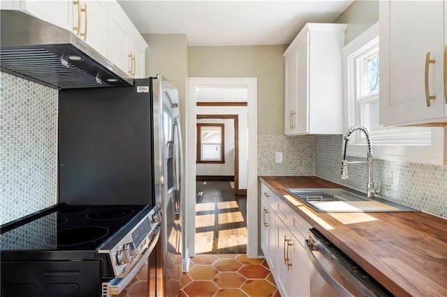 kitchen with a sink, extractor fan, appliances with stainless steel finishes, white cabinetry, and butcher block counters