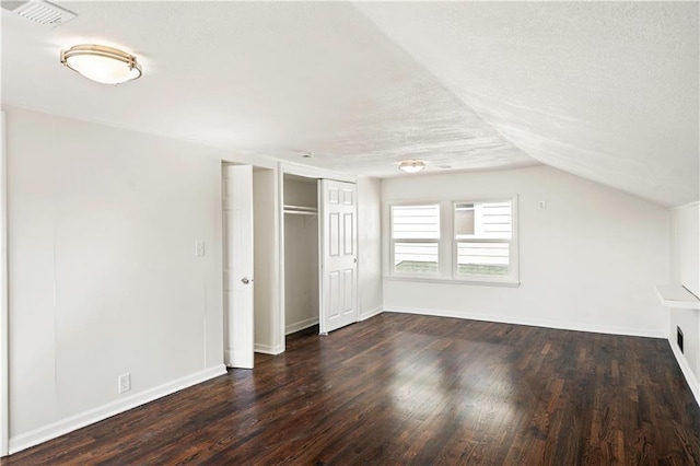 unfurnished bedroom featuring visible vents, a textured ceiling, lofted ceiling, and dark wood-style flooring