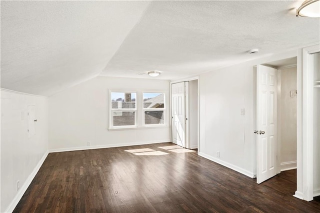 interior space featuring a textured ceiling, lofted ceiling, baseboards, and wood finished floors