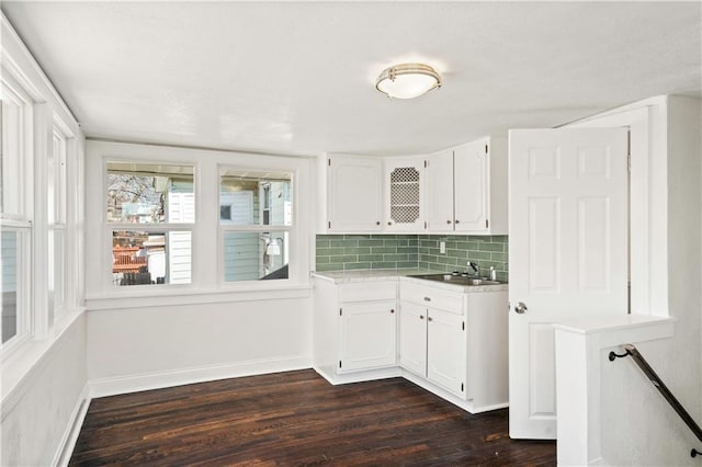 kitchen featuring baseboards, dark wood-style flooring, a sink, decorative backsplash, and white cabinets