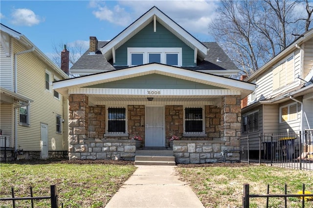 view of front of house with stone siding, a porch, a shingled roof, and fence