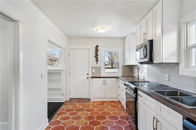 kitchen featuring dark countertops, stainless steel microwave, tasteful backsplash, range with electric stovetop, and white cabinets