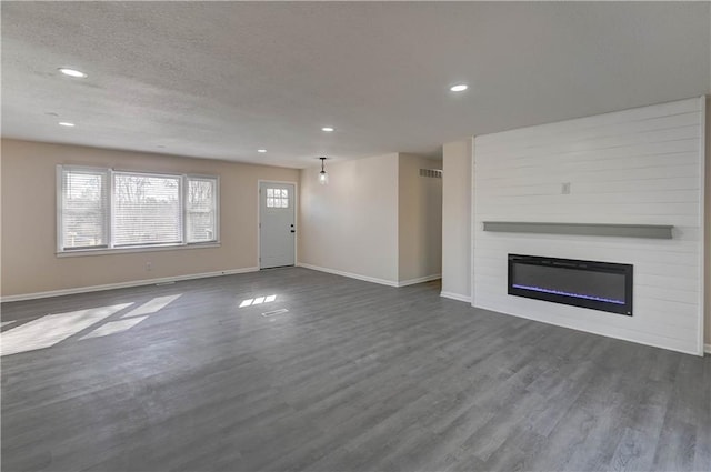 unfurnished living room with a textured ceiling, recessed lighting, a large fireplace, baseboards, and dark wood-style flooring