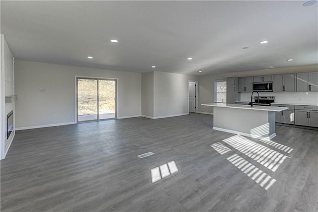 unfurnished living room with dark wood-style floors, recessed lighting, a large fireplace, and baseboards