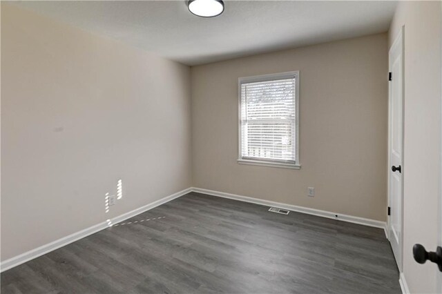 unfurnished room featuring visible vents, dark wood-type flooring, and baseboards