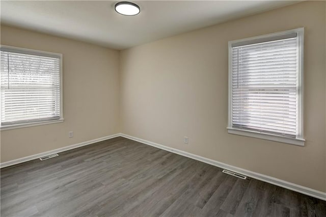 empty room featuring wood finished floors, baseboards, and visible vents