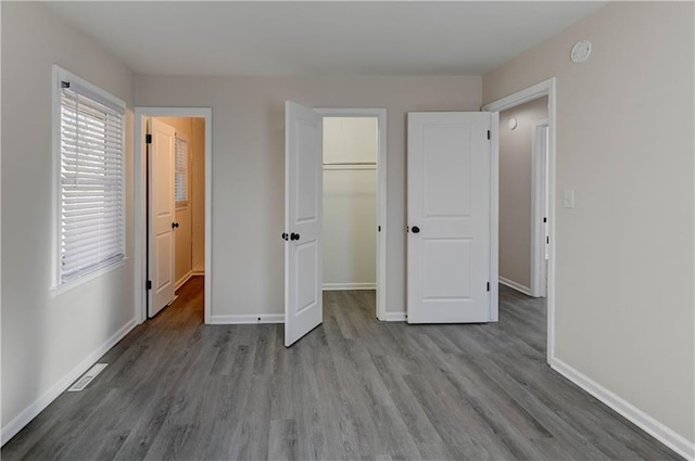 unfurnished bedroom with visible vents, baseboards, wood finished floors, and a spacious closet