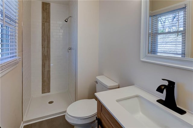 bathroom featuring a tile shower, toilet, and vanity