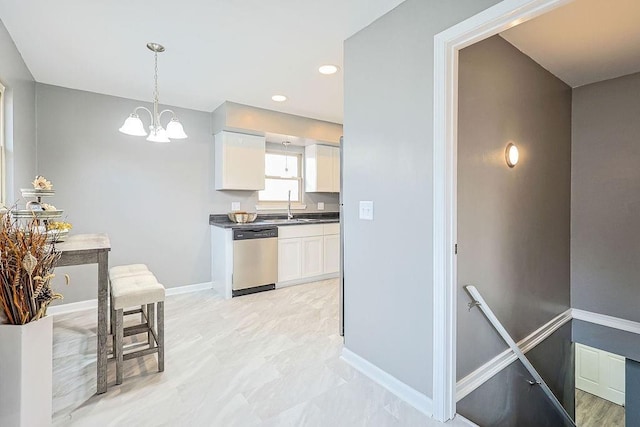 kitchen with dark countertops, stainless steel dishwasher, a notable chandelier, white cabinetry, and a sink