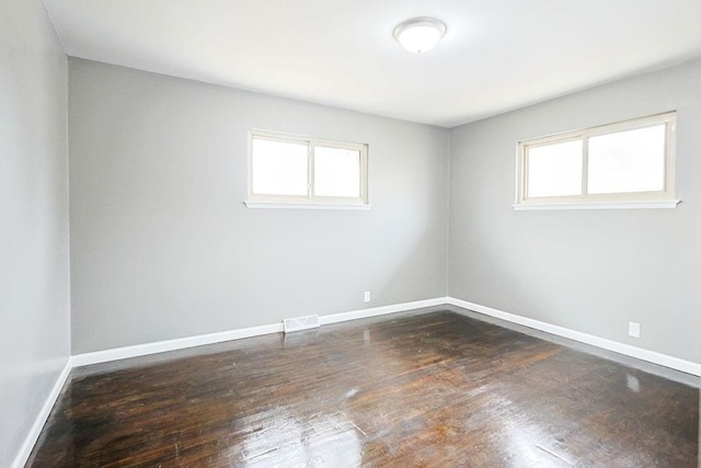 spare room featuring visible vents, baseboards, a healthy amount of sunlight, and hardwood / wood-style flooring