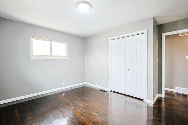 unfurnished bedroom with wood finished floors, visible vents, a closet, and baseboards