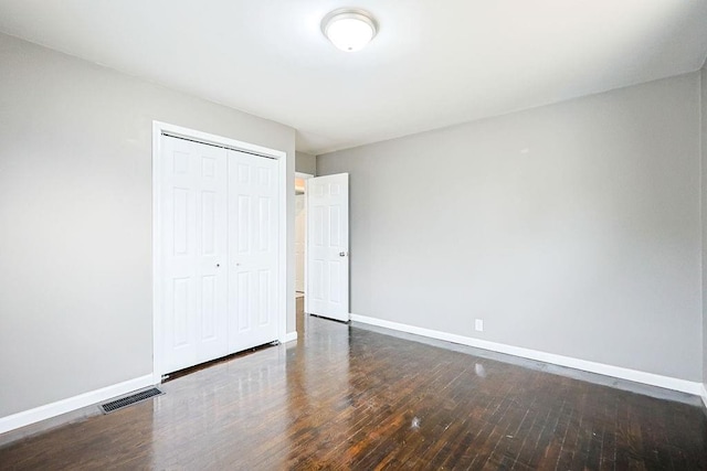 unfurnished bedroom with visible vents, baseboards, a closet, and hardwood / wood-style flooring