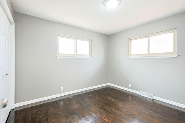 spare room with dark wood finished floors, baseboards, visible vents, and a wealth of natural light