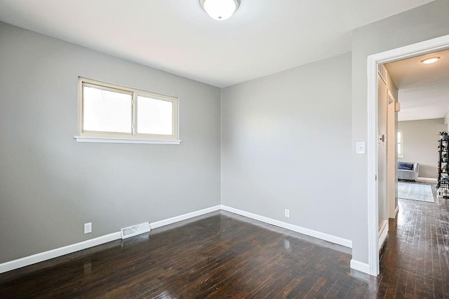 unfurnished room featuring dark wood-style floors, visible vents, and baseboards