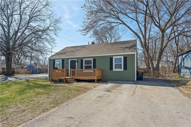 view of front of property with a wooden deck, a chimney, a front lawn, and a shingled roof