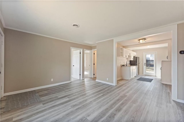 unfurnished living room with visible vents, baseboards, a sink, crown molding, and light wood-type flooring