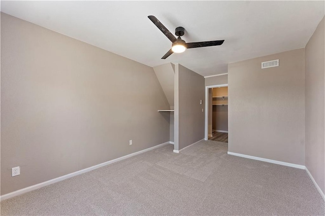 unfurnished bedroom featuring visible vents, light carpet, a walk in closet, a ceiling fan, and baseboards