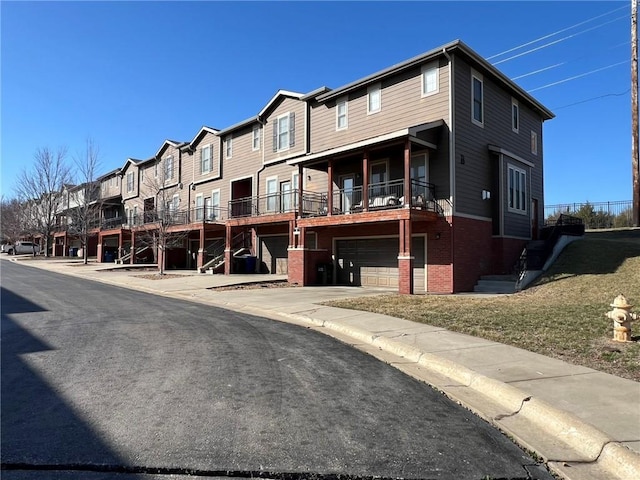 exterior space featuring a garage, a residential view, brick siding, and concrete driveway