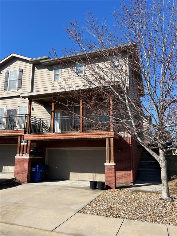 view of front of property featuring brick siding, driveway, an attached garage, and a balcony