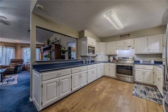 kitchen with under cabinet range hood, stainless steel appliances, dark countertops, and white cabinets