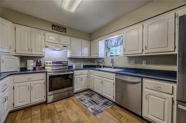 kitchen featuring light wood-type flooring, under cabinet range hood, a sink, white cabinetry, and appliances with stainless steel finishes