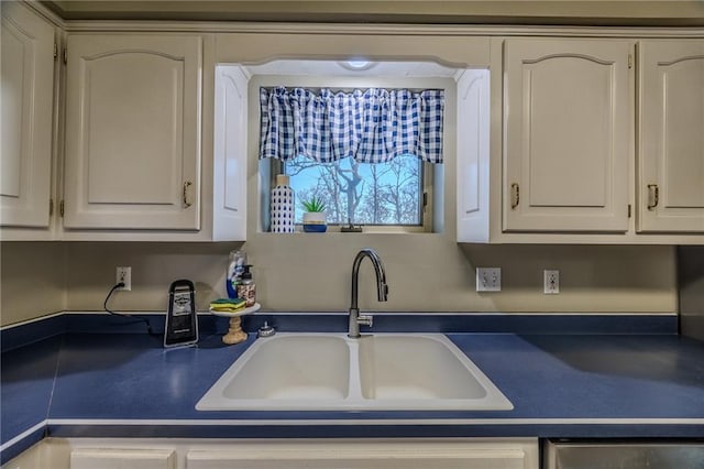 kitchen featuring dark countertops, white cabinetry, stainless steel dishwasher, and a sink