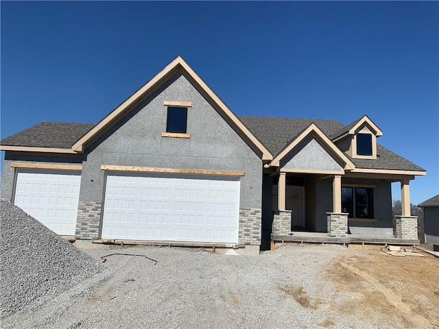 view of front of property featuring stucco siding, a porch, roof with shingles, an attached garage, and brick siding